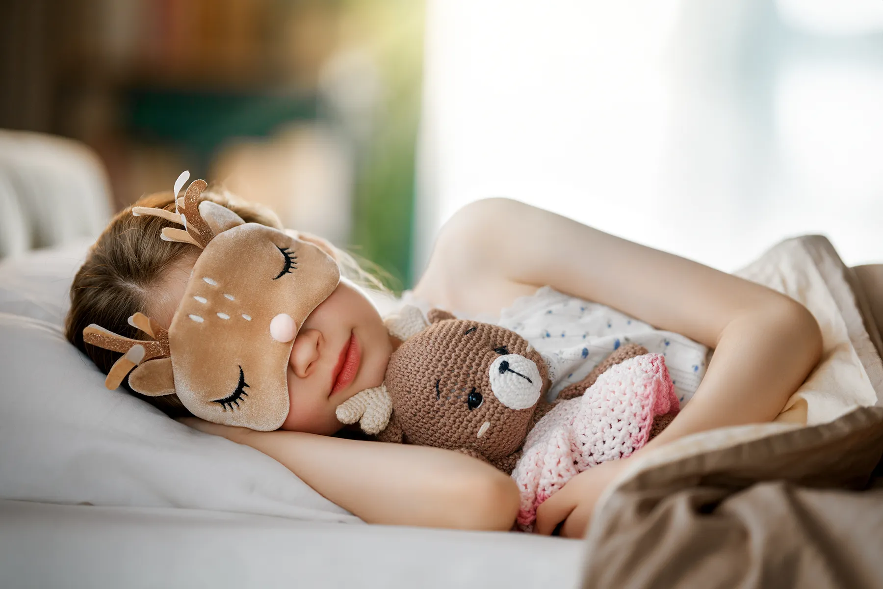 child-sleeping-with-deer-mask-and-teddy-bear-happy-bun-peds. Child sleeping in bed wearing a deer sleep mask and holding a teddy bear.