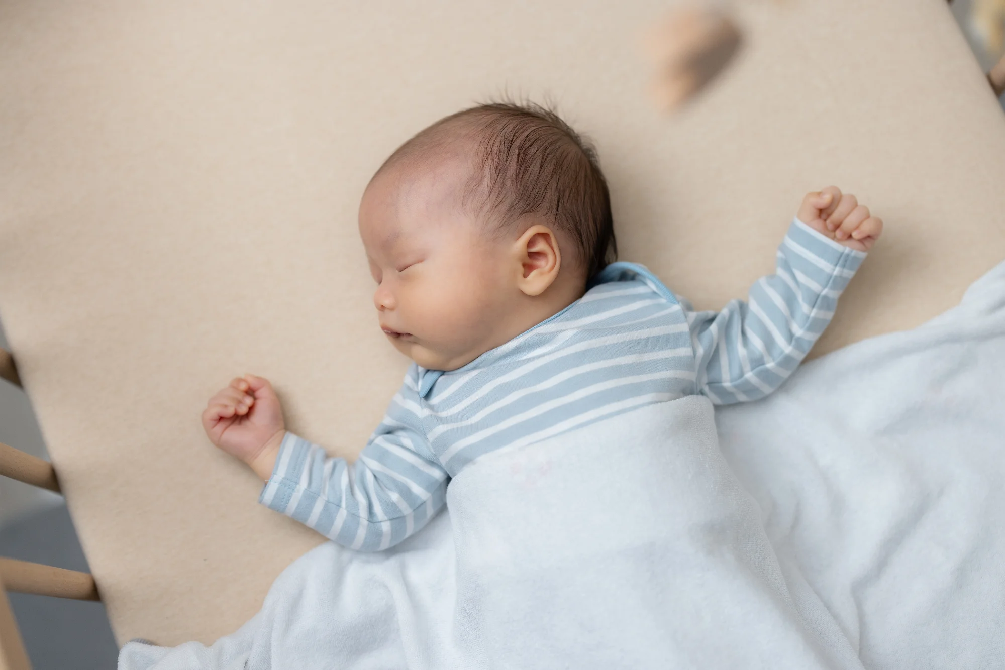 Newborn sleeping peacefully on back in crib wearing blue striped onesie