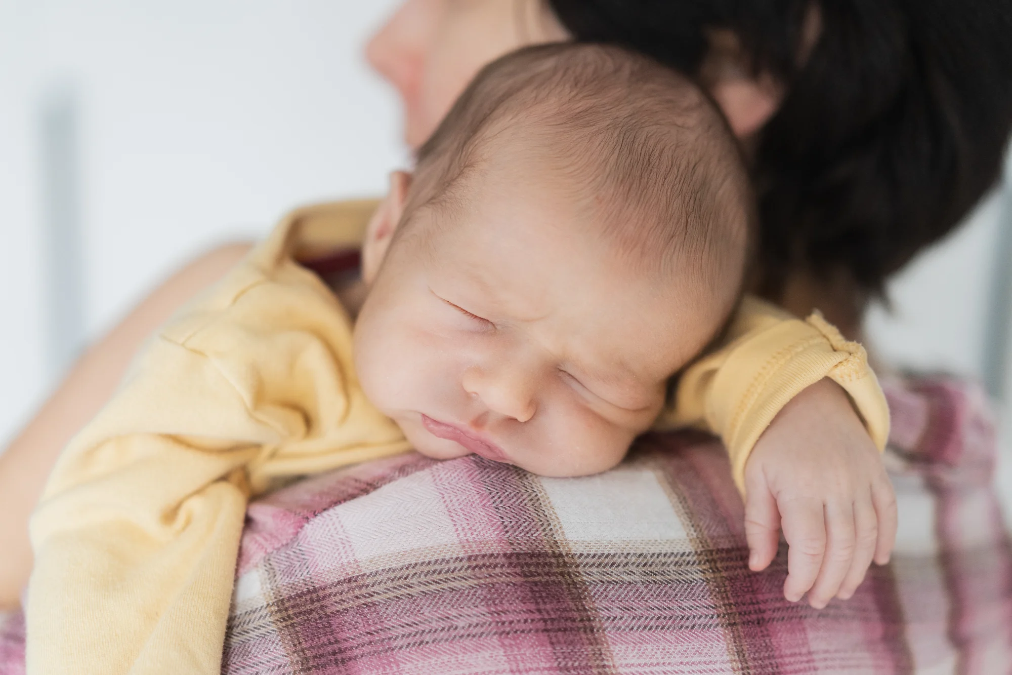Sleeping newborn in a yellow onesie resting peacefully on a parent's shoulder
